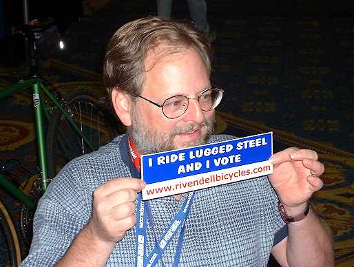 John Schubert holding bumper sticker reading "I ride lugged steel and I vote."